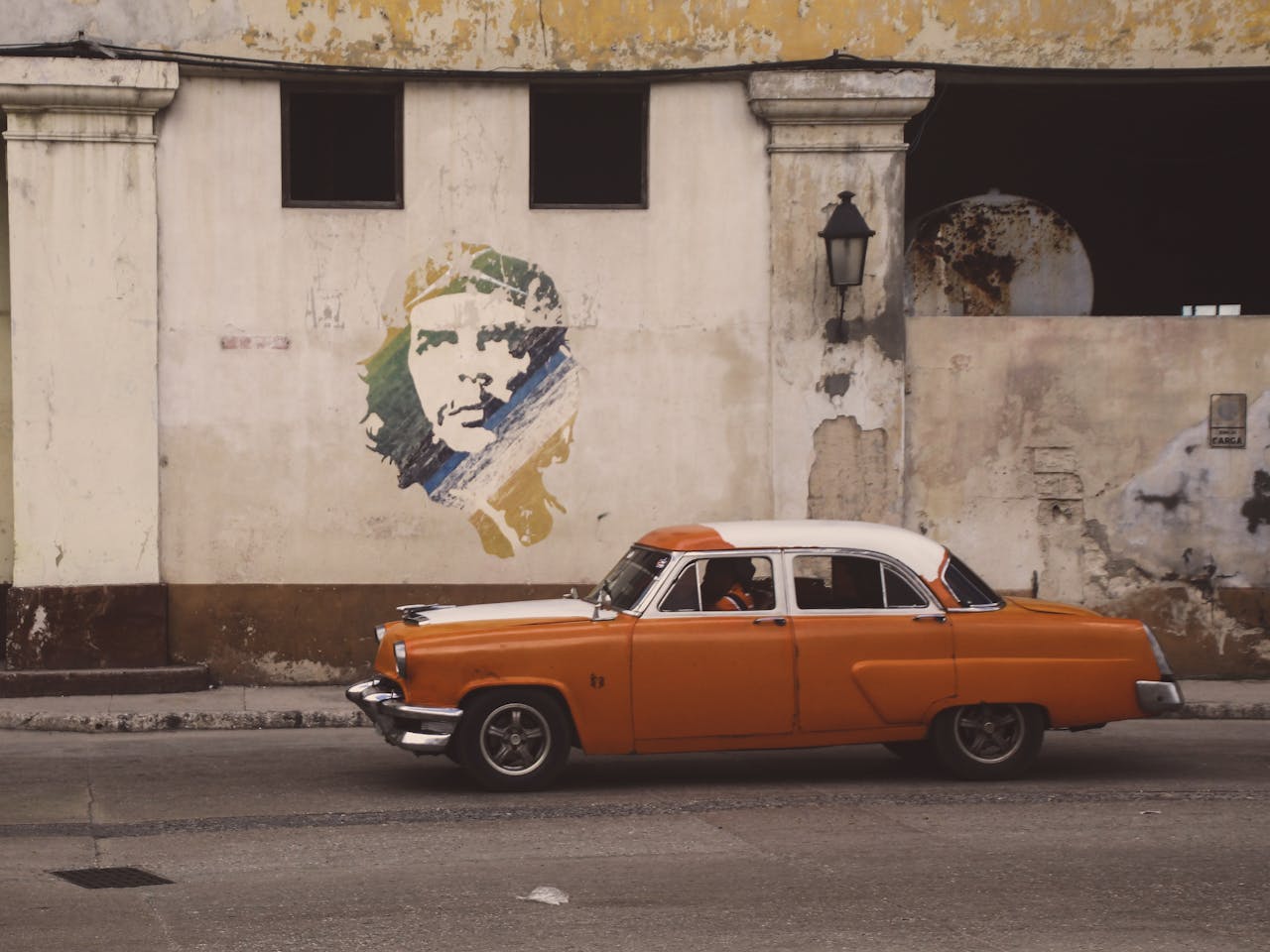 Vintage GAZ-21 car in Havana against a mural background, capturing Cuban street life.