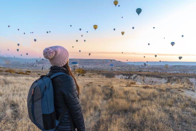Woman watching hot air balloons in Cappadocia at sunrise, a popular travel destination.