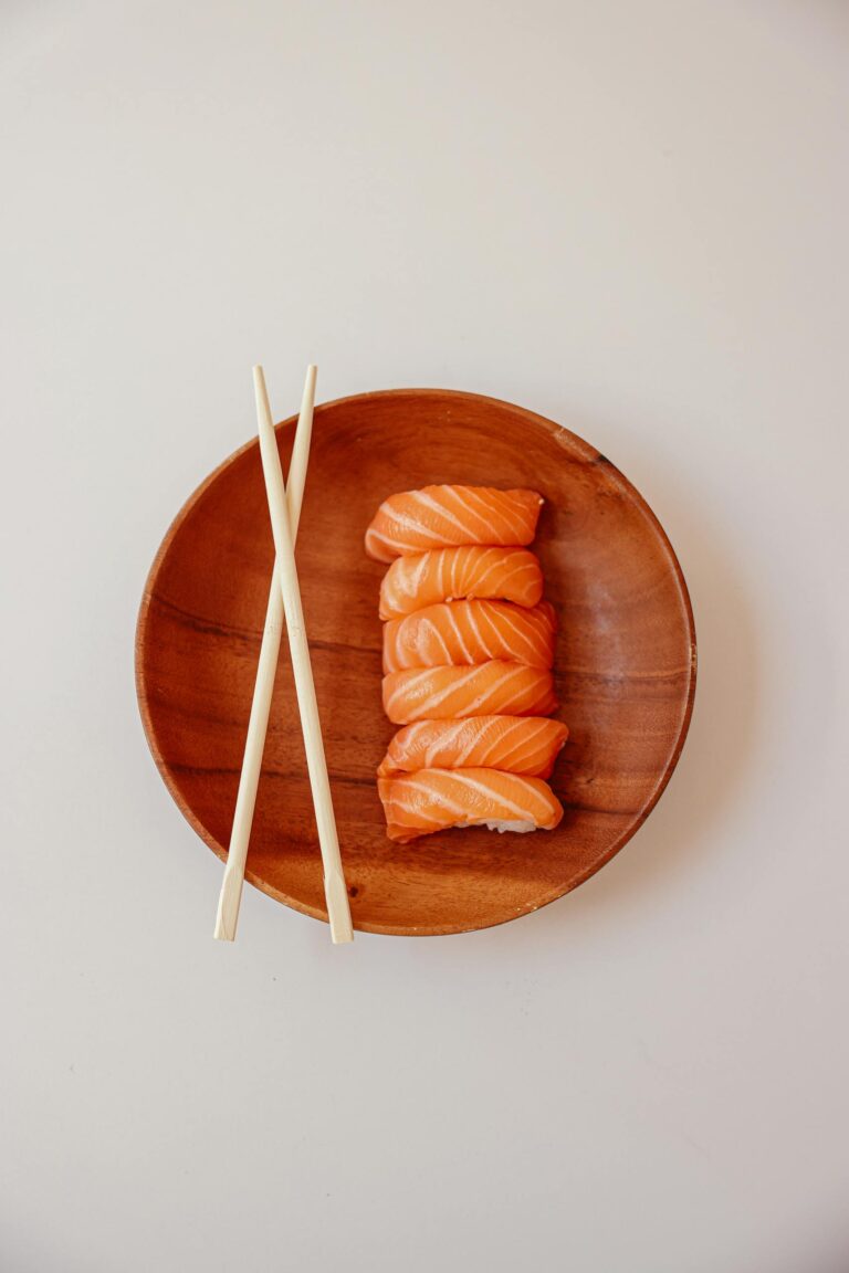 Minimalist top view of fresh salmon sushi on a wooden plate with chopsticks.