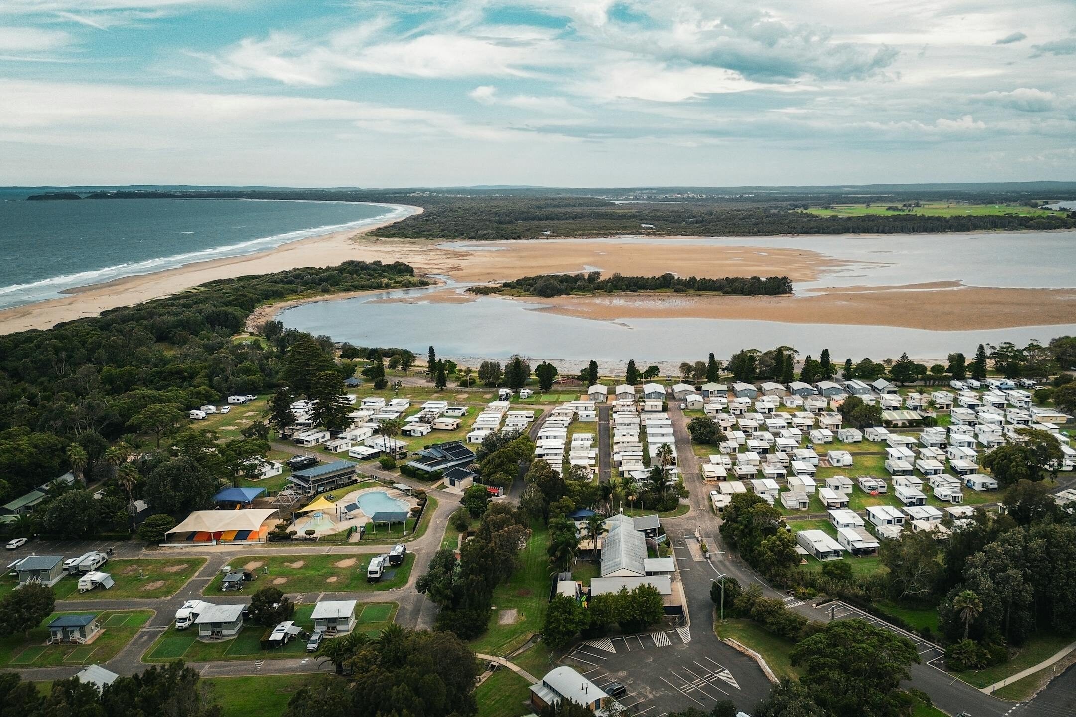 Aerial view of Gerroa, New South Wales showcasing a vibrant caravan park by the beach.